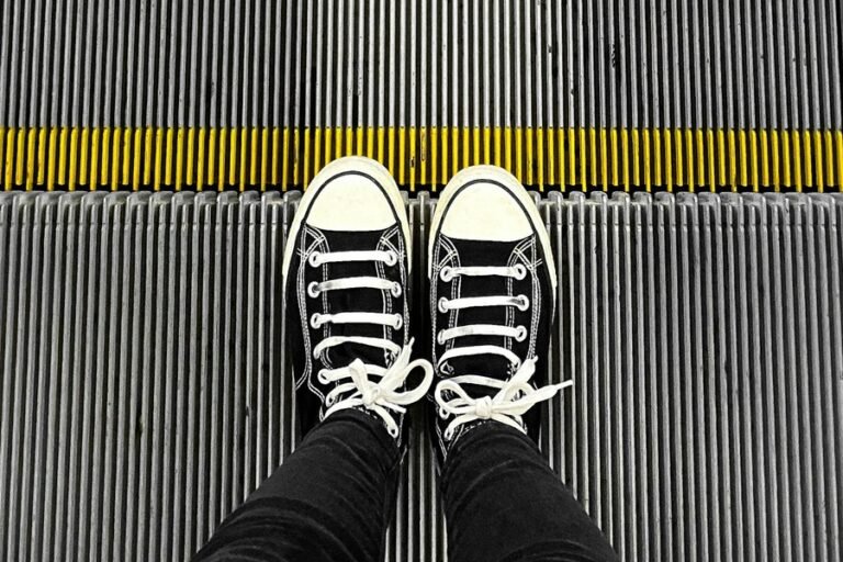 a picture of a young person's feet wearing converse standing at the top of an escalator