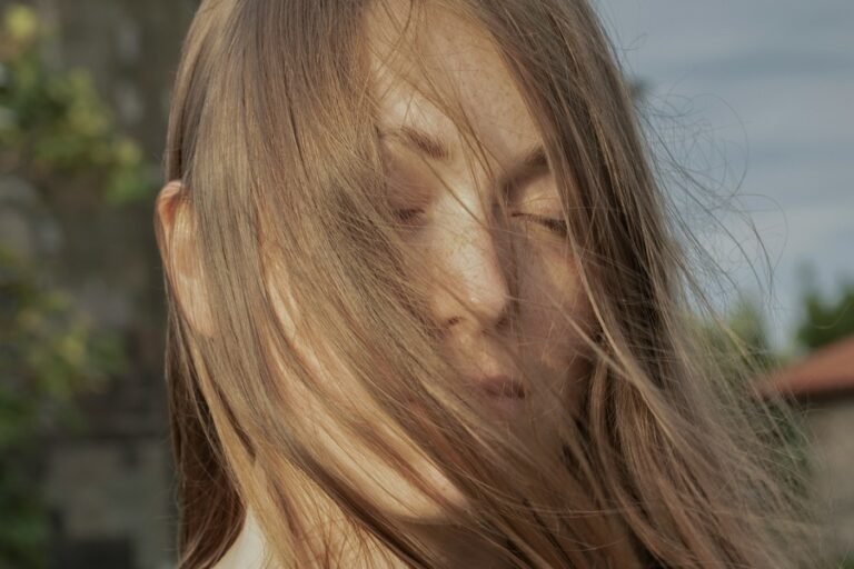 woman outside with the wind blowing her hair gently over her face, her eyes are closed