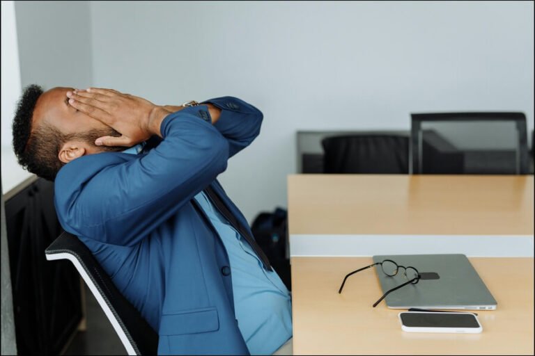 Man sitting at desk in an office leaning back with his head in his hands