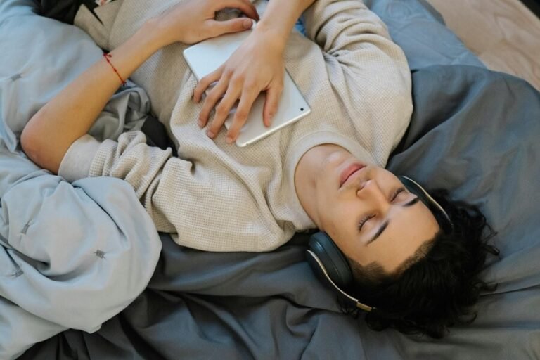 young man lying on a bed with a table listening to music on headphones