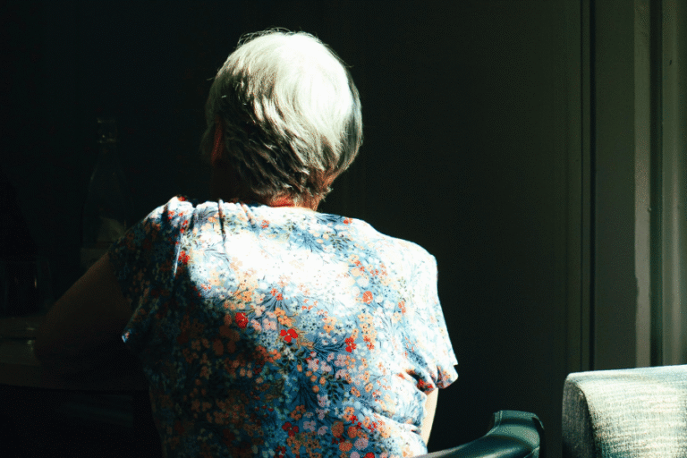 Alzheimers lady facing away in chair sitting in shadow