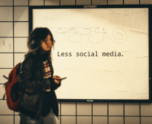 A young girl holding a mobile phone walking past a notice board with the wording less social media on it.
